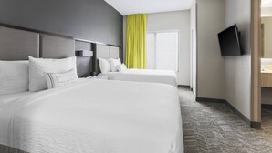 Habitación de hotel con dos camas, un televisor de pantalla plana montado en la pared, un ventanal con cortinas amarillas y piso alfombrado.