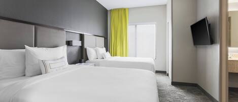 Habitación de hotel con dos camas, un televisor de pantalla plana montado en la pared, un ventanal con cortinas amarillas y piso alfombrado.