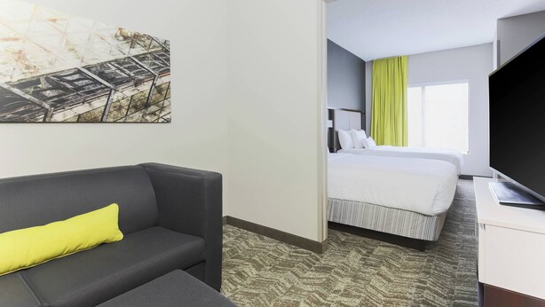 A hotel room with a grey sofa, a bed with white bedding, a television on a white stand, and a painting on the wall. - SpringHill Suites by Marriott Austin Parmer/Tech Ridge (Austin)