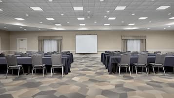 A conference room with a large screen, multiple tables, and chairs arranged for a meeting.