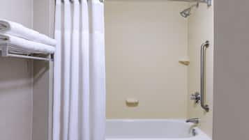 A bathroom with a bathtub, a shower with a grab bar, and a towel rack with folded towels.