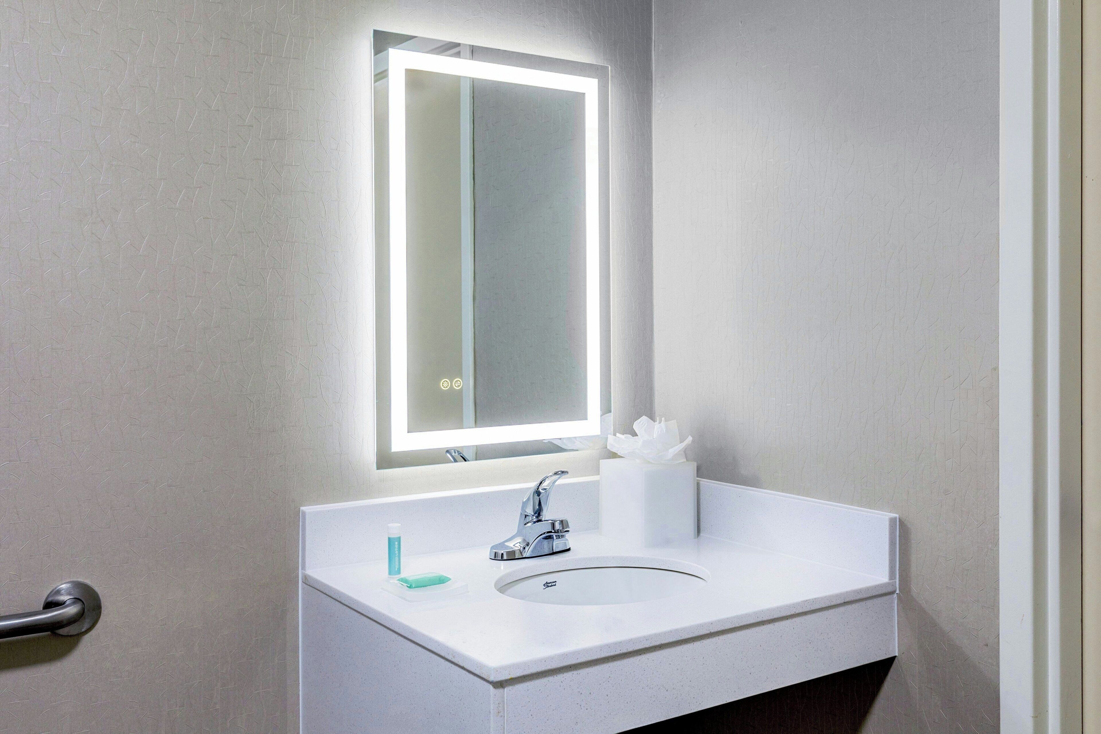 A bathroom with a white sink, a mirror with integrated lighting, and a towel dispenser.