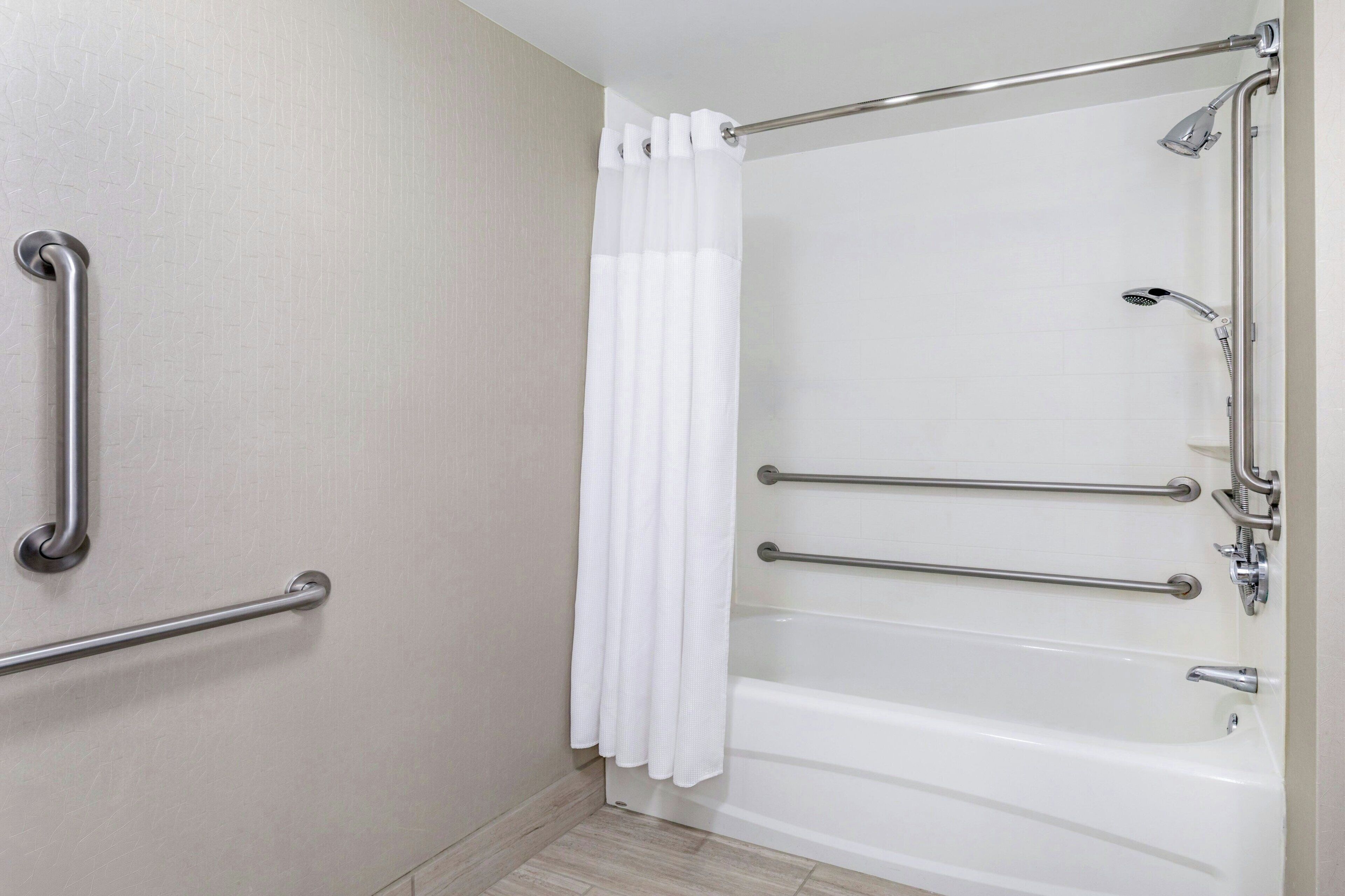 A bathroom with a bathtub, grab bars, and a shower head.