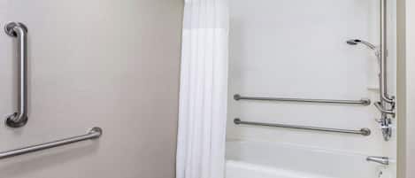 A bathroom with a bathtub, grab bars, and a shower head.