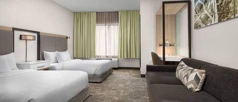 Habitación de hotel con dos camas, un sofá, un escritorio y un espejo grande.