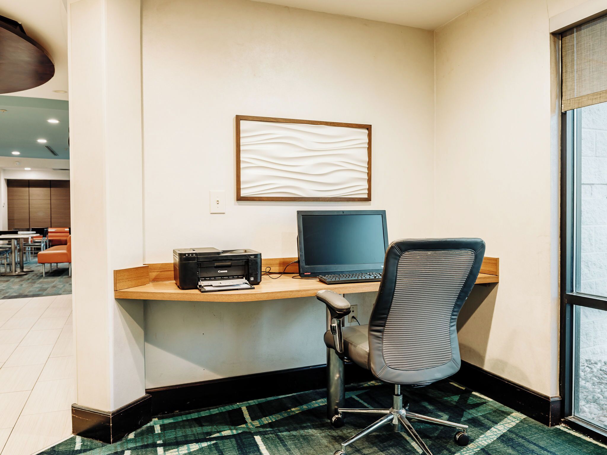 Een hotelkantoor met een bureau, stoel, printer en computer.