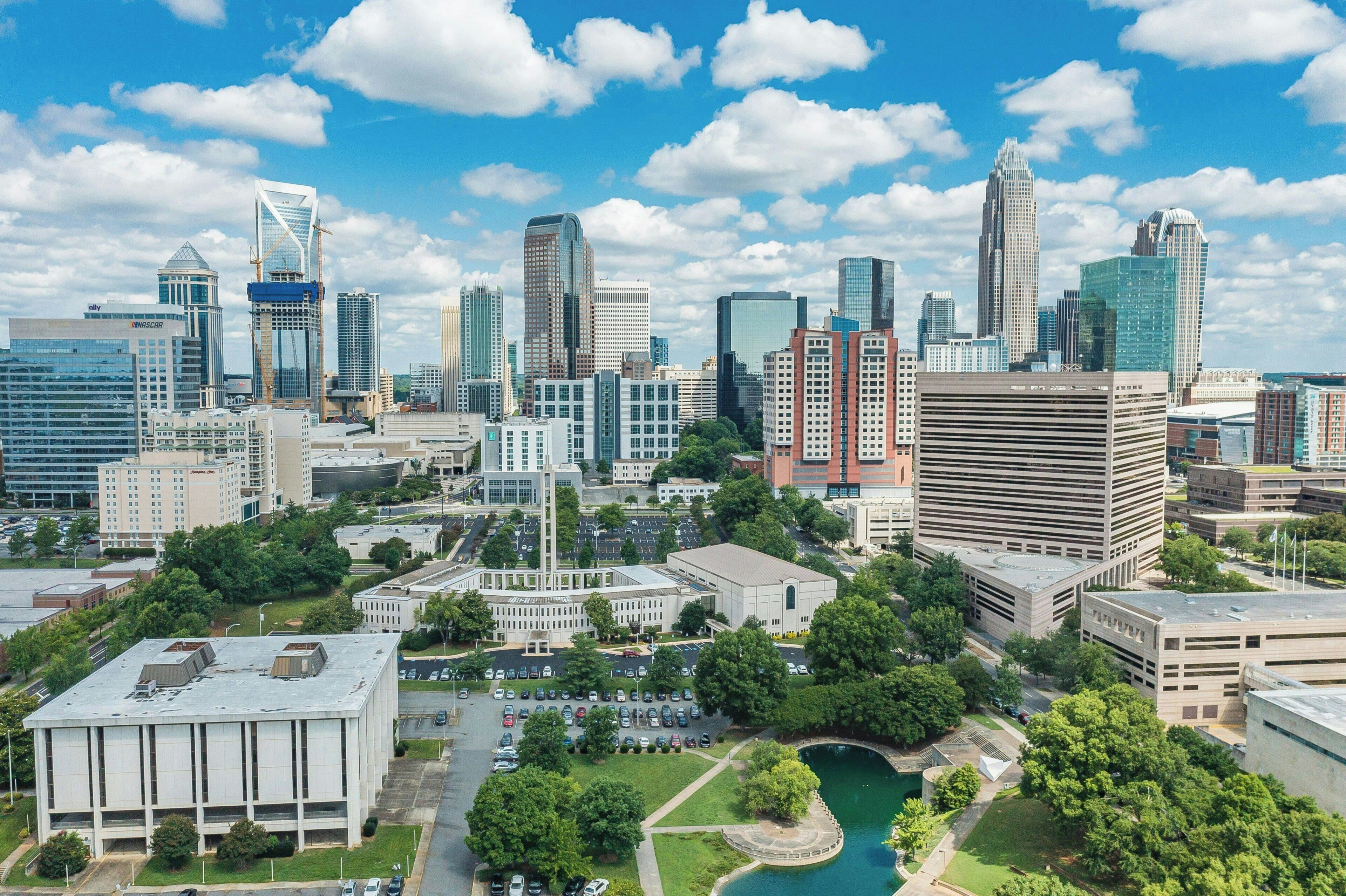 A cityscape with various buildings, including a prominent skyscraper, a parking lot, and a green area with trees.