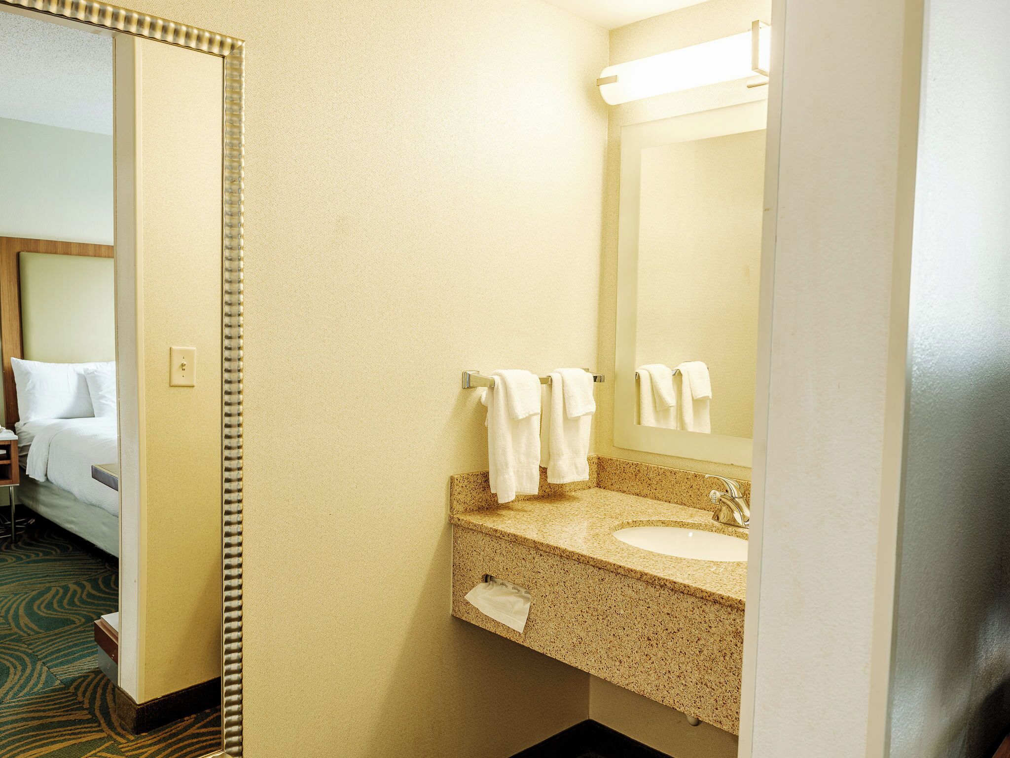 A hotel bathroom with a sink, mirror, and towel rack.