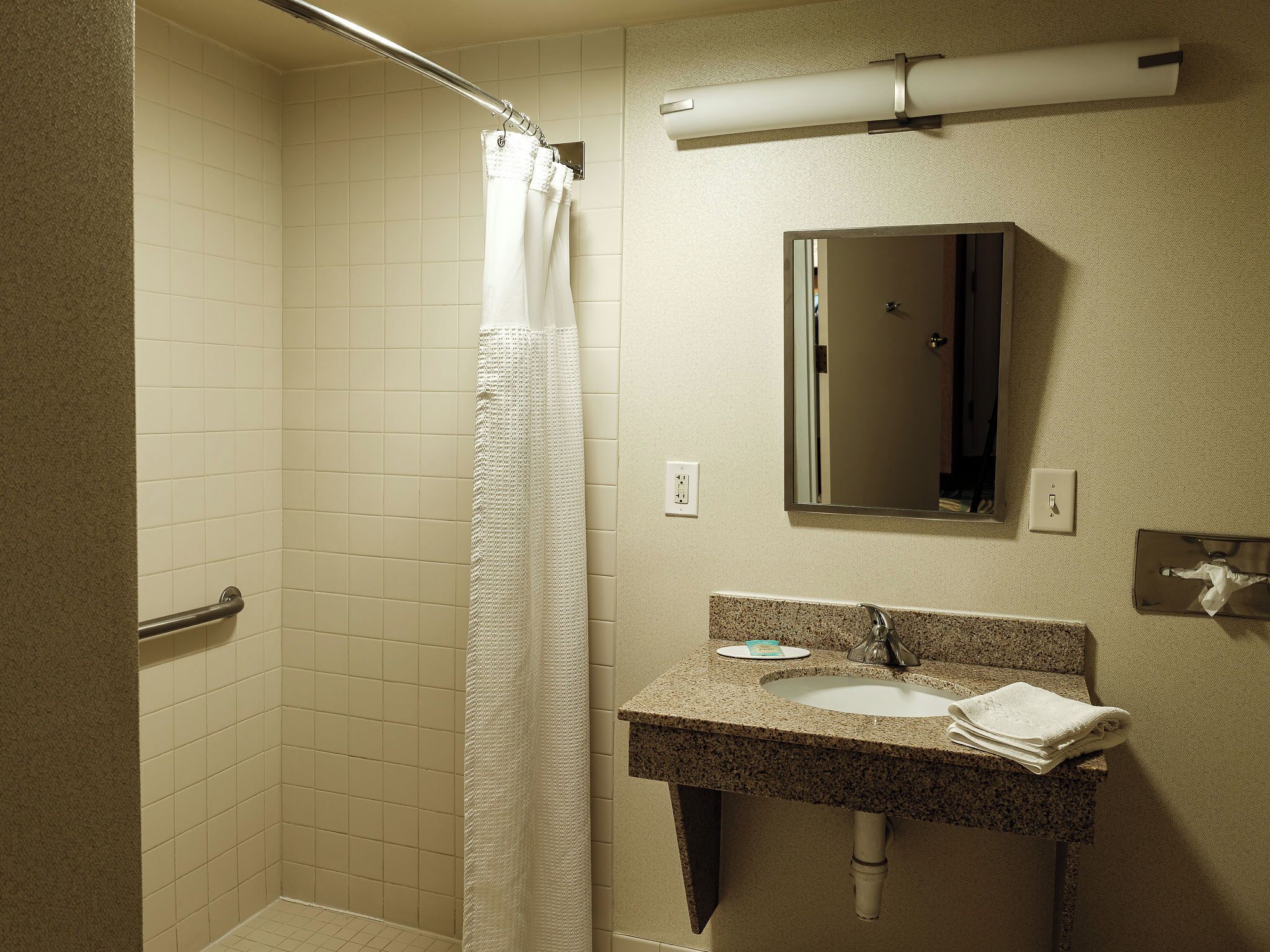 A bathroom with a shower, a sink, a mirror, and a towel rack.