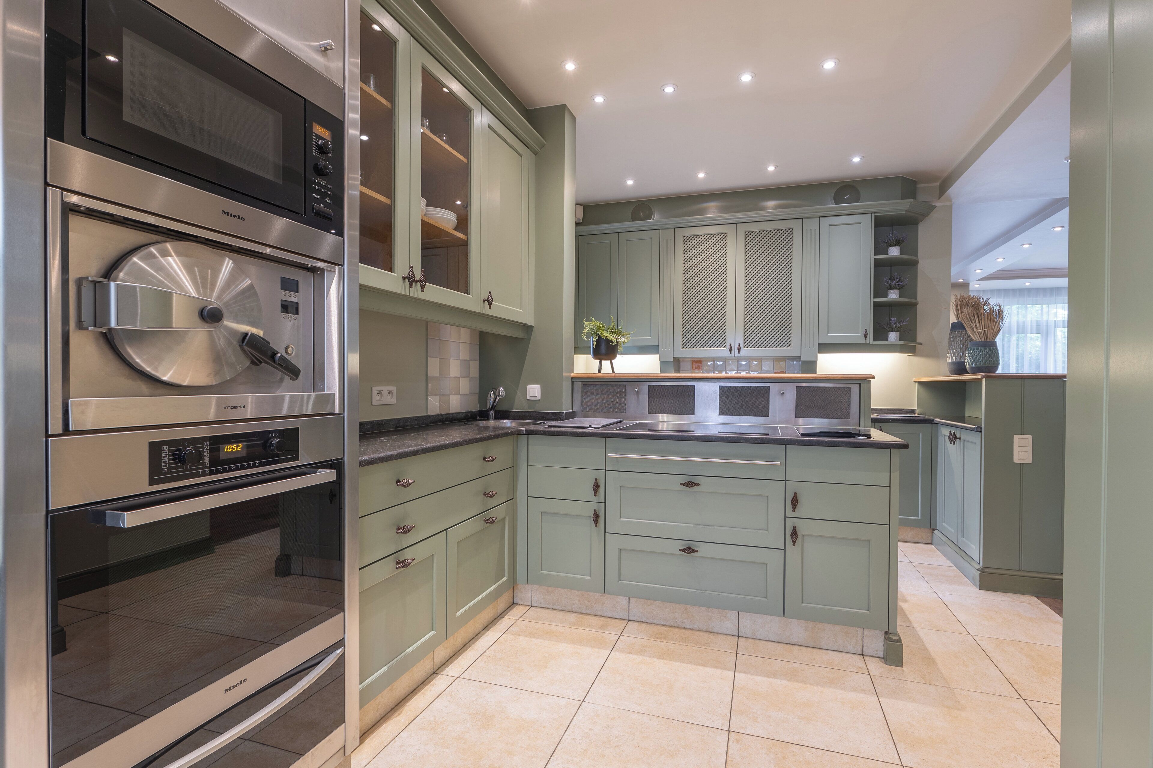 A modern kitchen with stainless steel appliances, green cabinetry, and a central island.