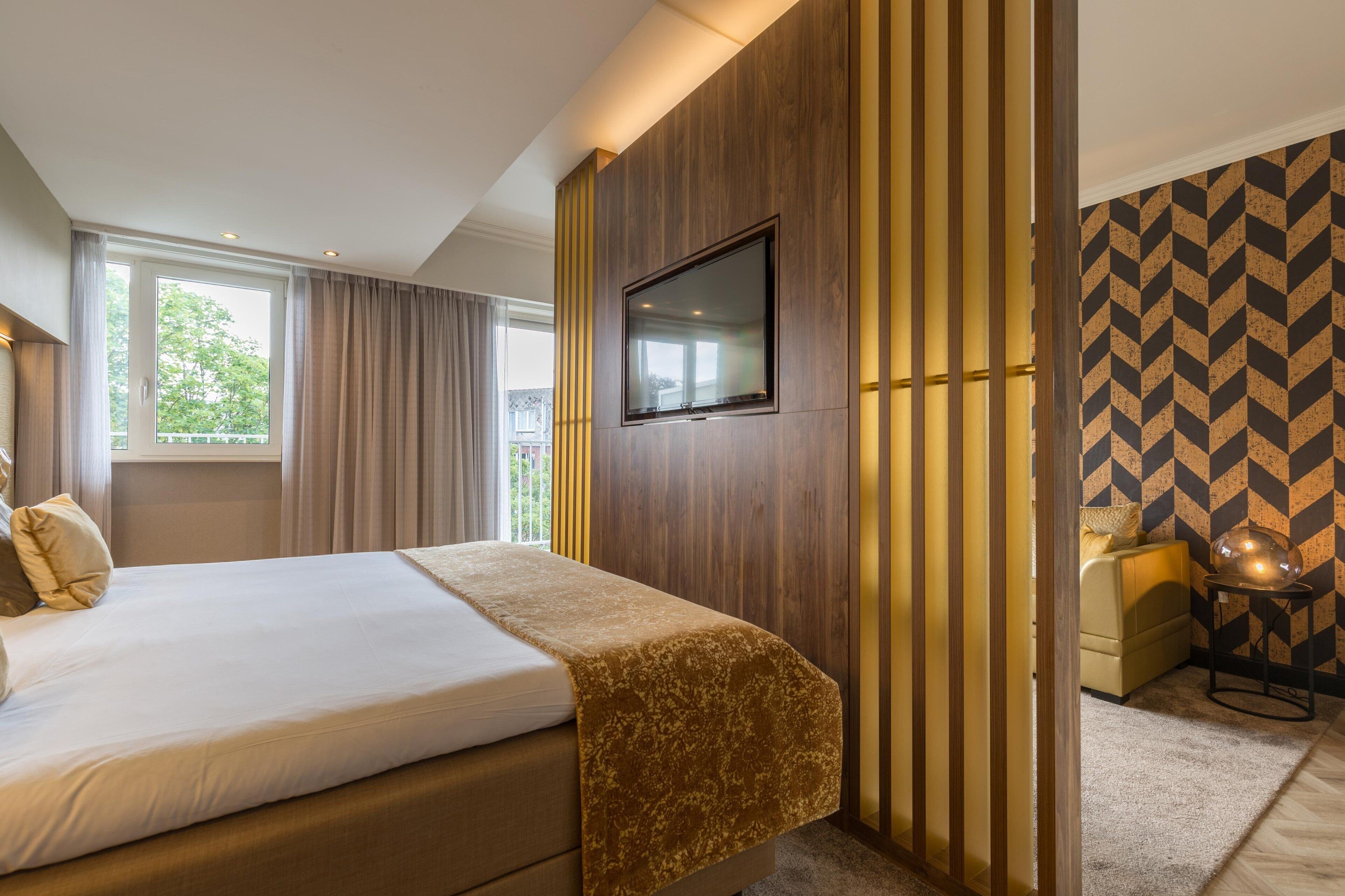 Una habitación de hotel con una cama grande, un televisor montado en la pared y un papel tapiz estampado.