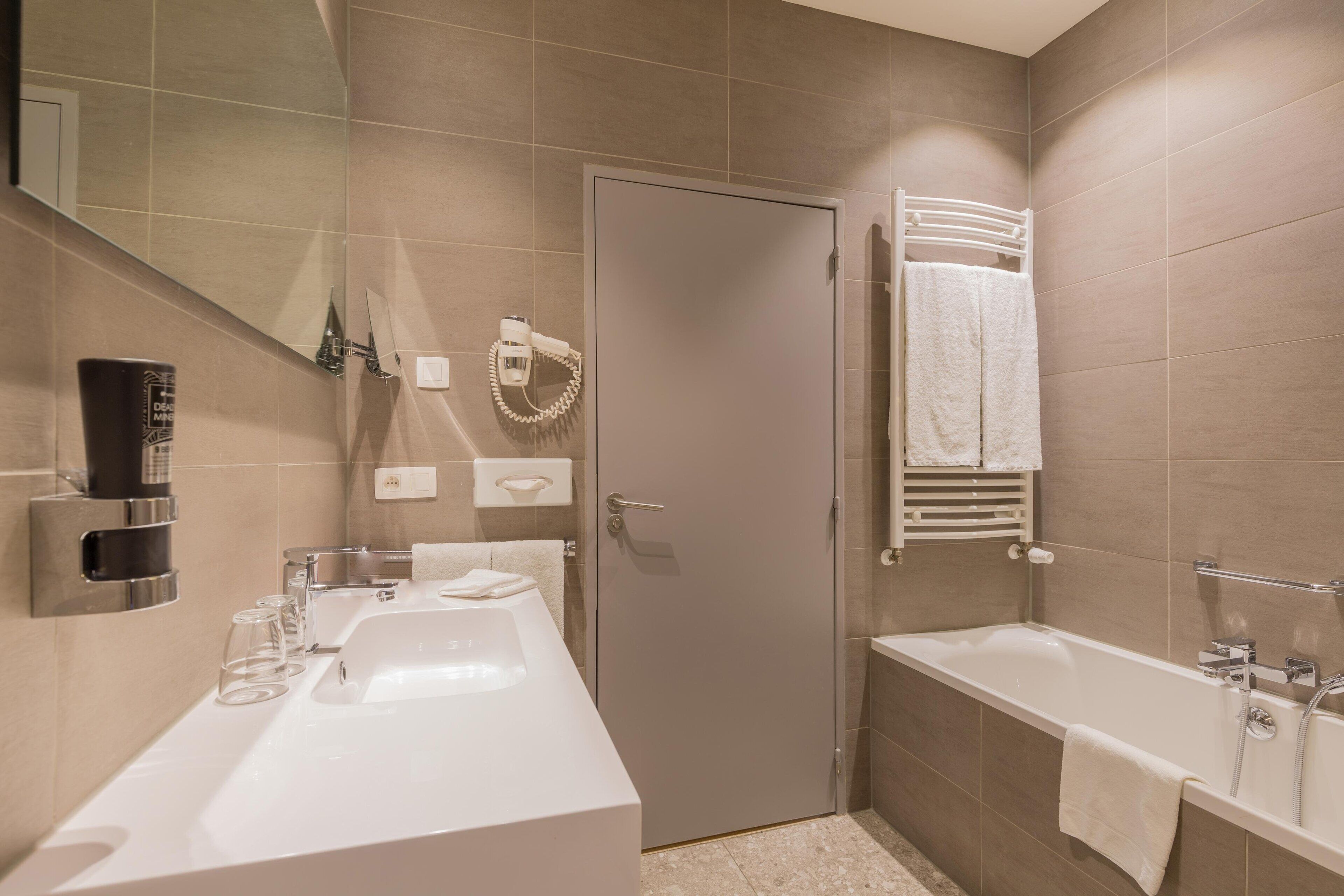 Een moderne badkamer met een groot wastafel, een badkuip en een douche. Er is een handdoekhouder en een spiegel aan de muur.
