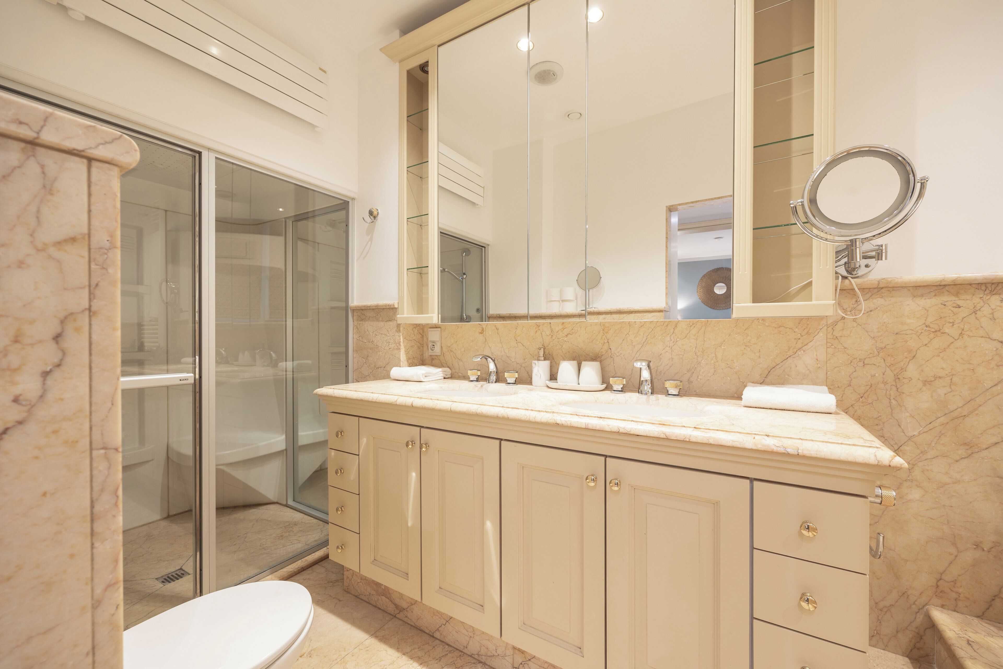Un ba ño con encimera de mármol, cabina de ducha de vidrio y un espejo grande.