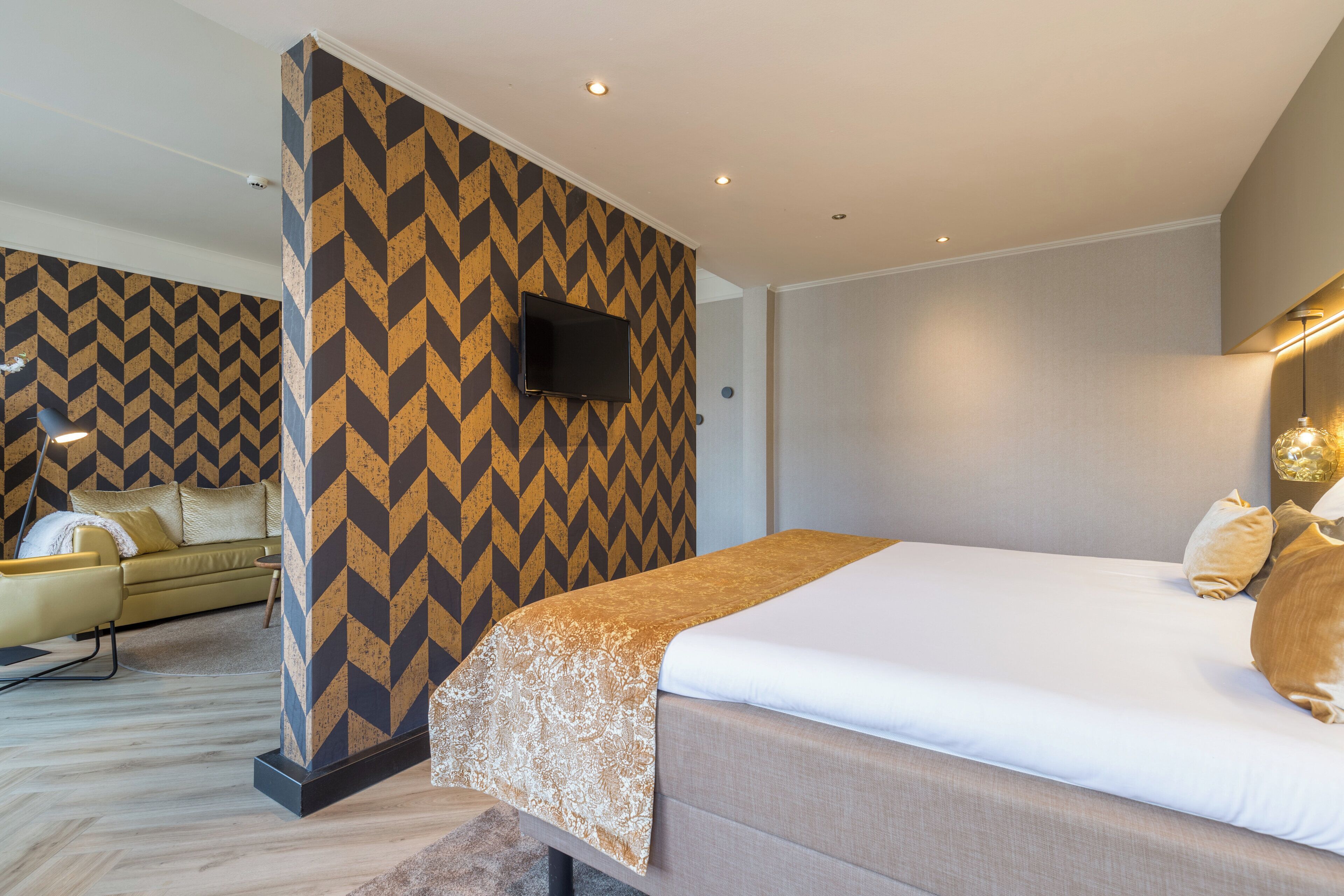Une chambre d’hôtel moderne avec un grand lit, un canapé, un téléviseur fixé au mur et un papier peint à motifs.