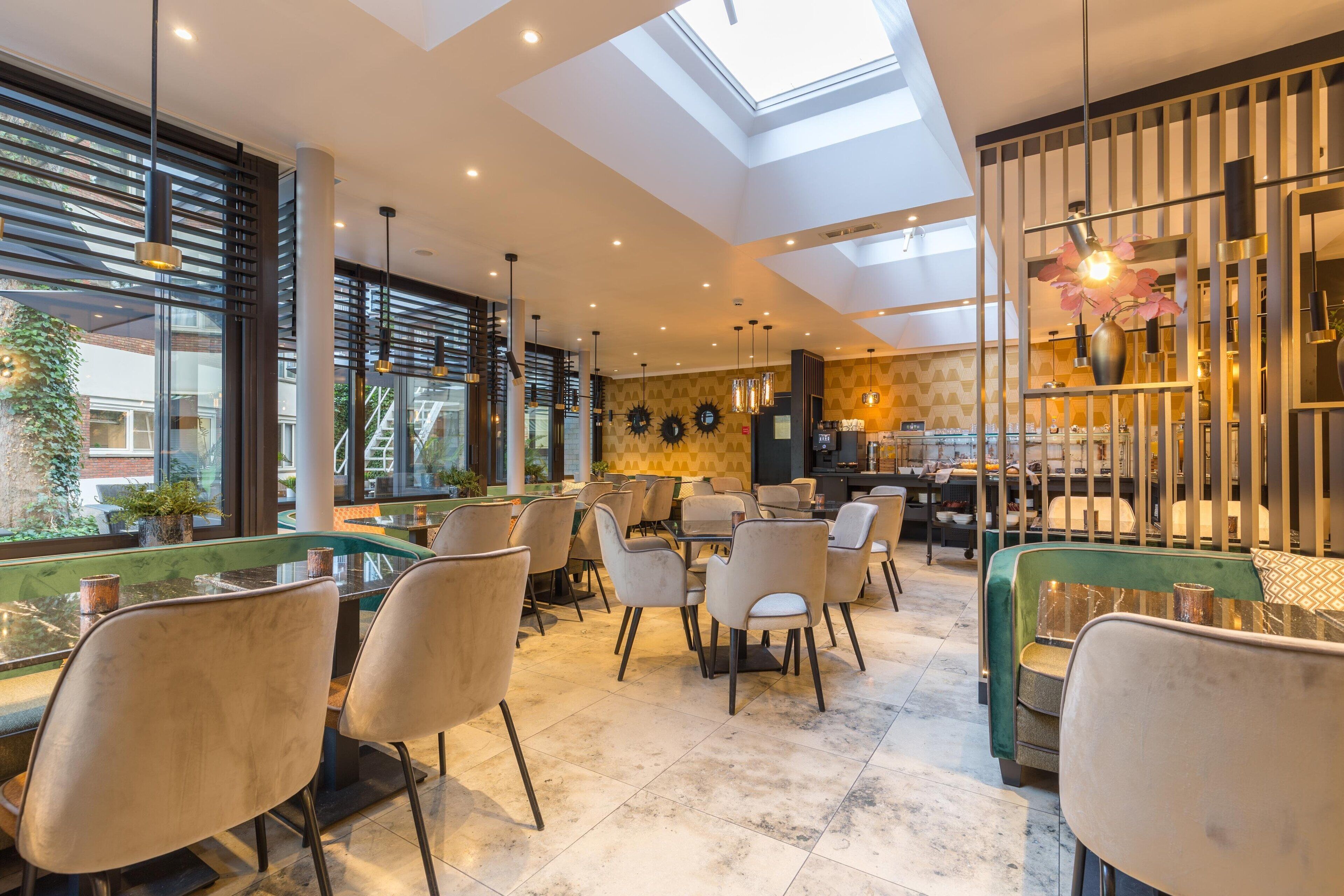 A modern restaurant with a high ceiling, skylight, and a mix of seating including tables and sofas.