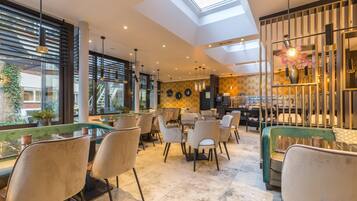 A modern restaurant with a high ceiling, skylight, and a mix of seating including tables and sofas.