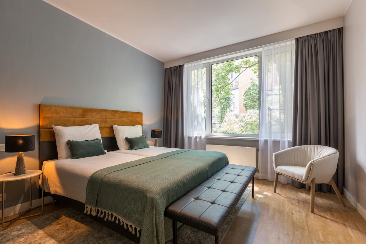 Une chambre à coucher bien rangée, avec un grand lit, une table de chevet avec une lampe, un banc et une chaise.