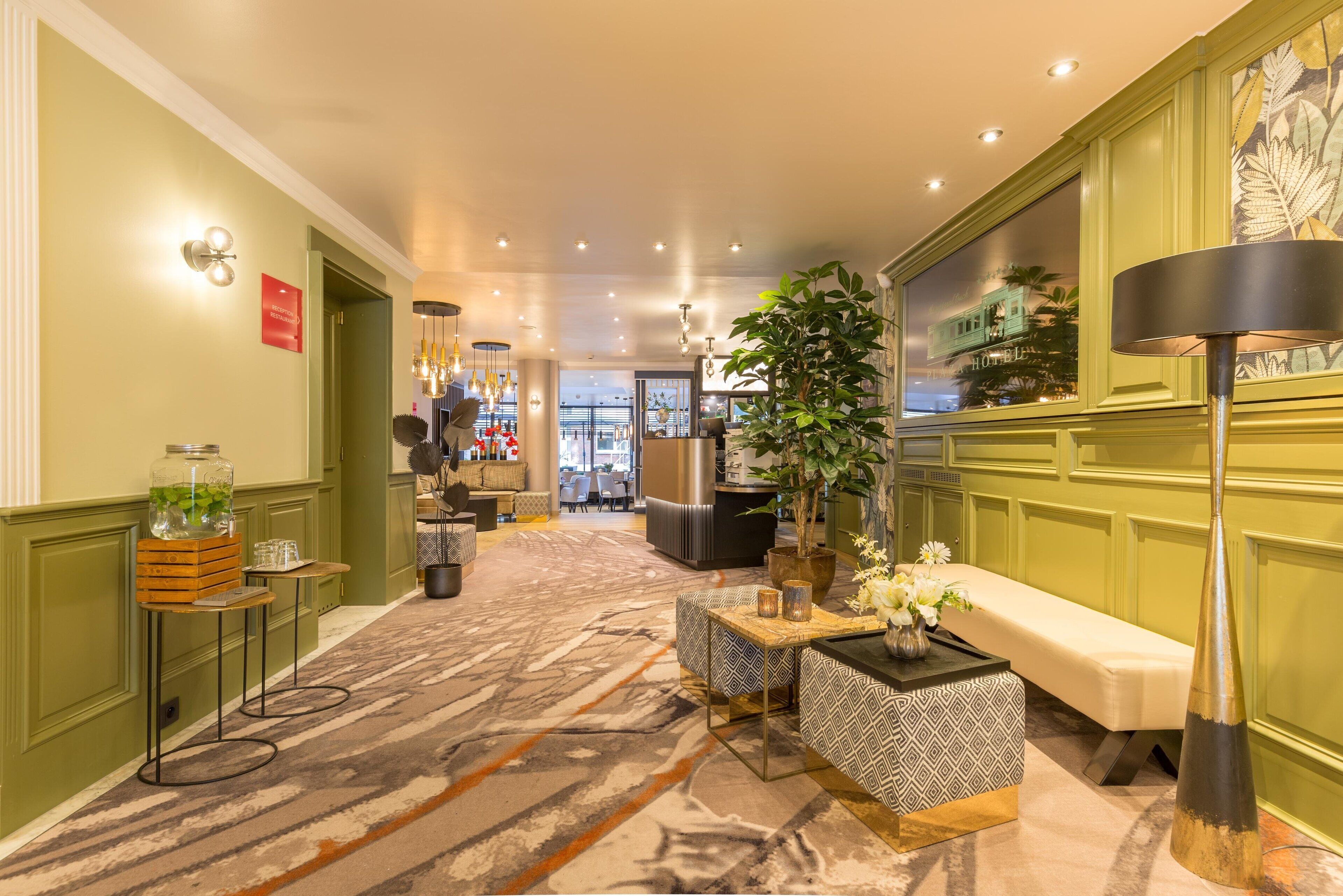 En hotellobby med ett mönstrat golv, en receptionsdisk, en bänk och en stor krukväxt.