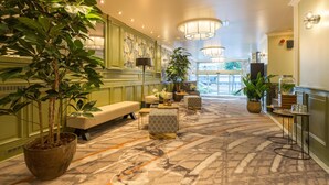 Un vestíbulo de hotel con alfombra estampada, zonas de estar y plantas en macetas.