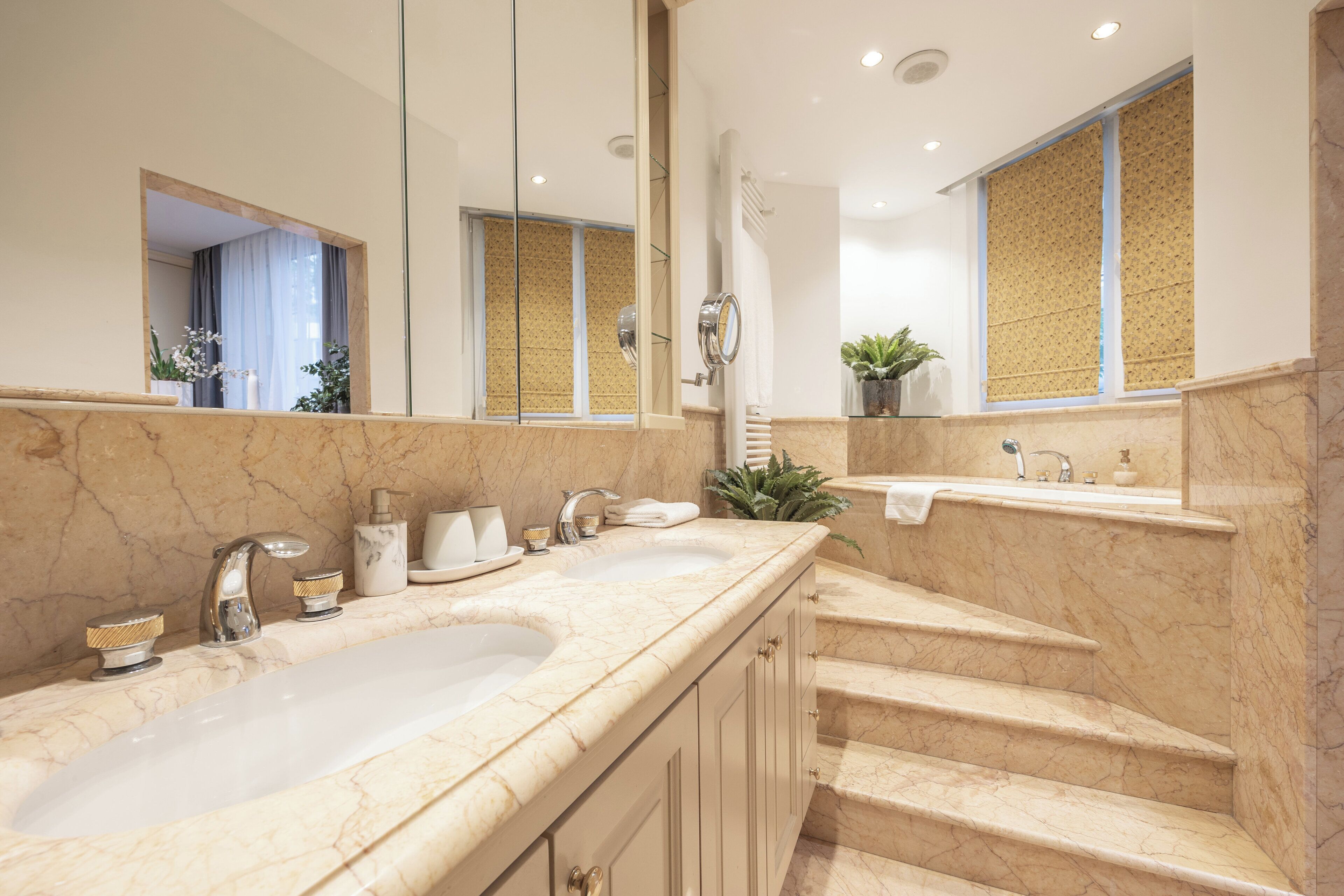 A bathroom with a double sink, a mirror, and a staircase leading to an upper level.