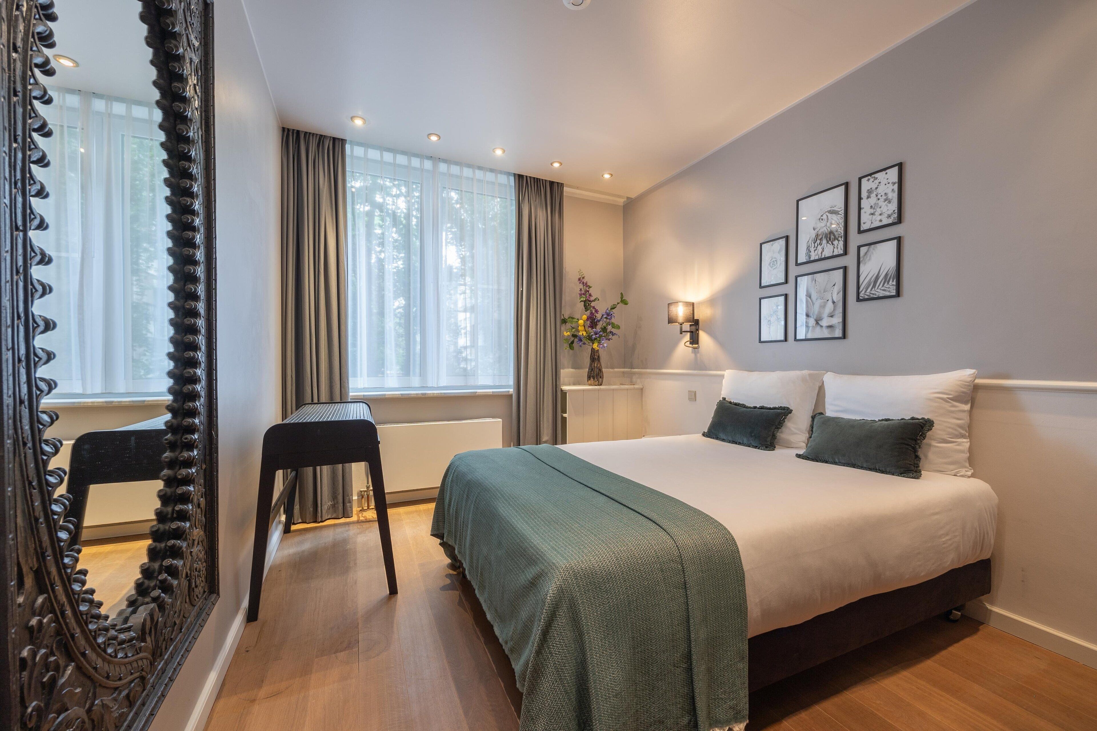 A bedroom with a large bed, a chair, a mirror, and a window with curtains.