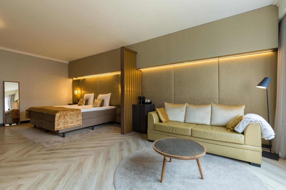 A modern hotel room with a bed, sofa, and round coffee table.