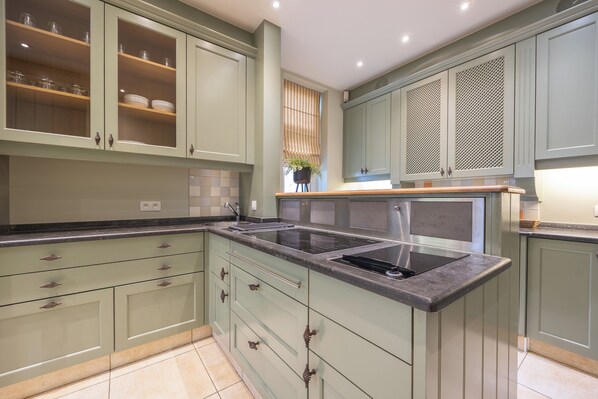 Una cocina moderna con armarios verde claro, una isla central con un lavamanos y una ventana con persianas.