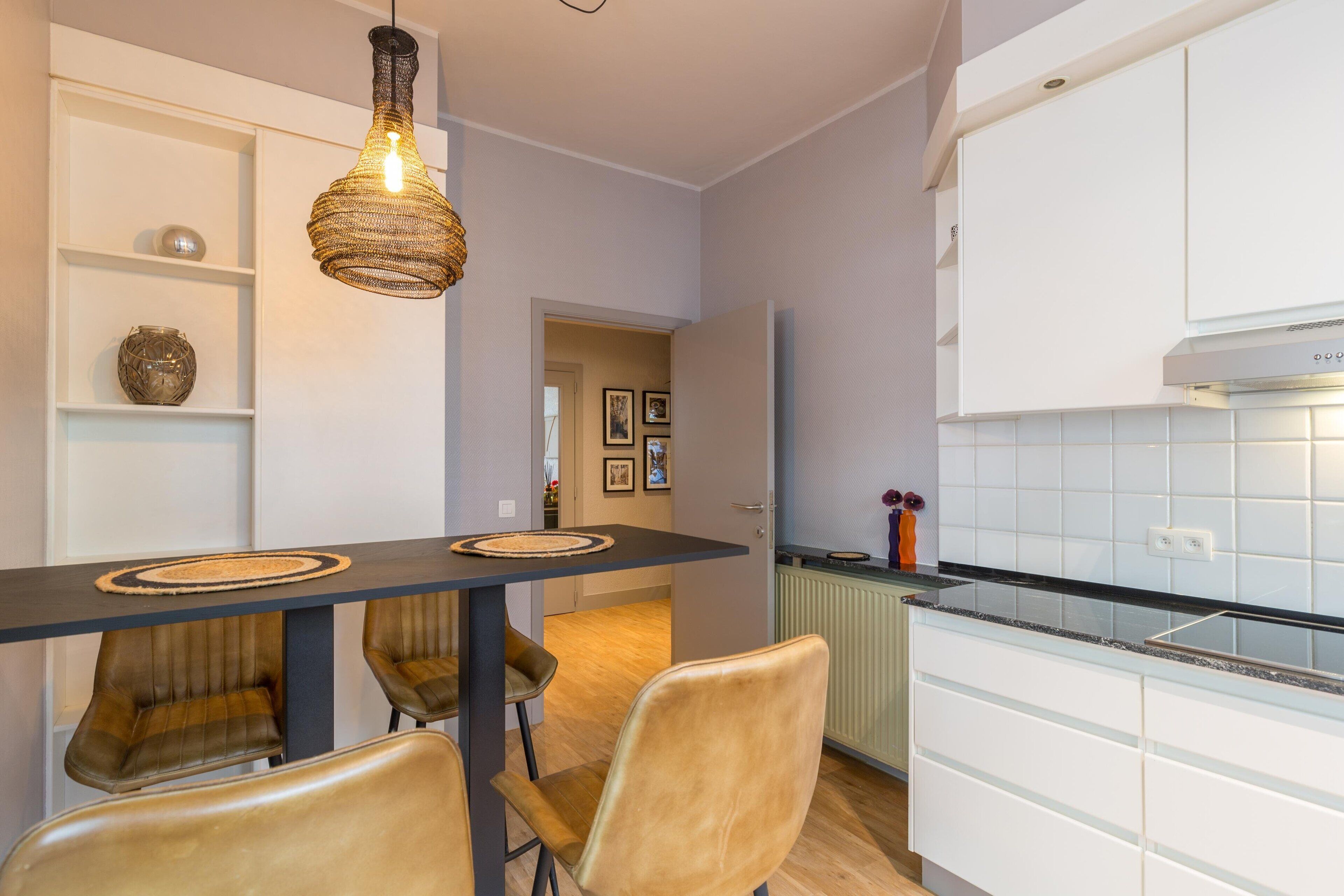 Une cuisine moderne avec des armoires blanches, un comptoir noir et un luminaire suspendu.