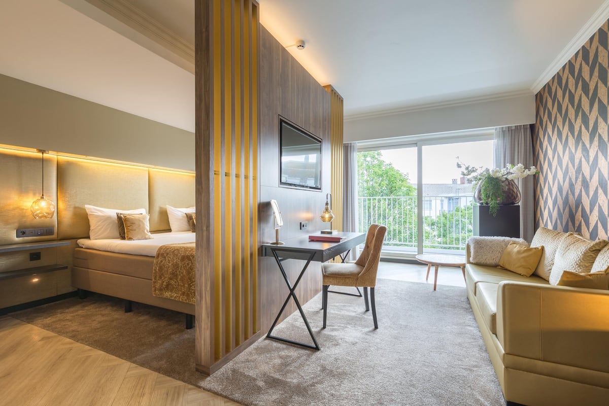 A modern bedroom with a bed, desk, and chair, a large window, and a view of the outdoors.