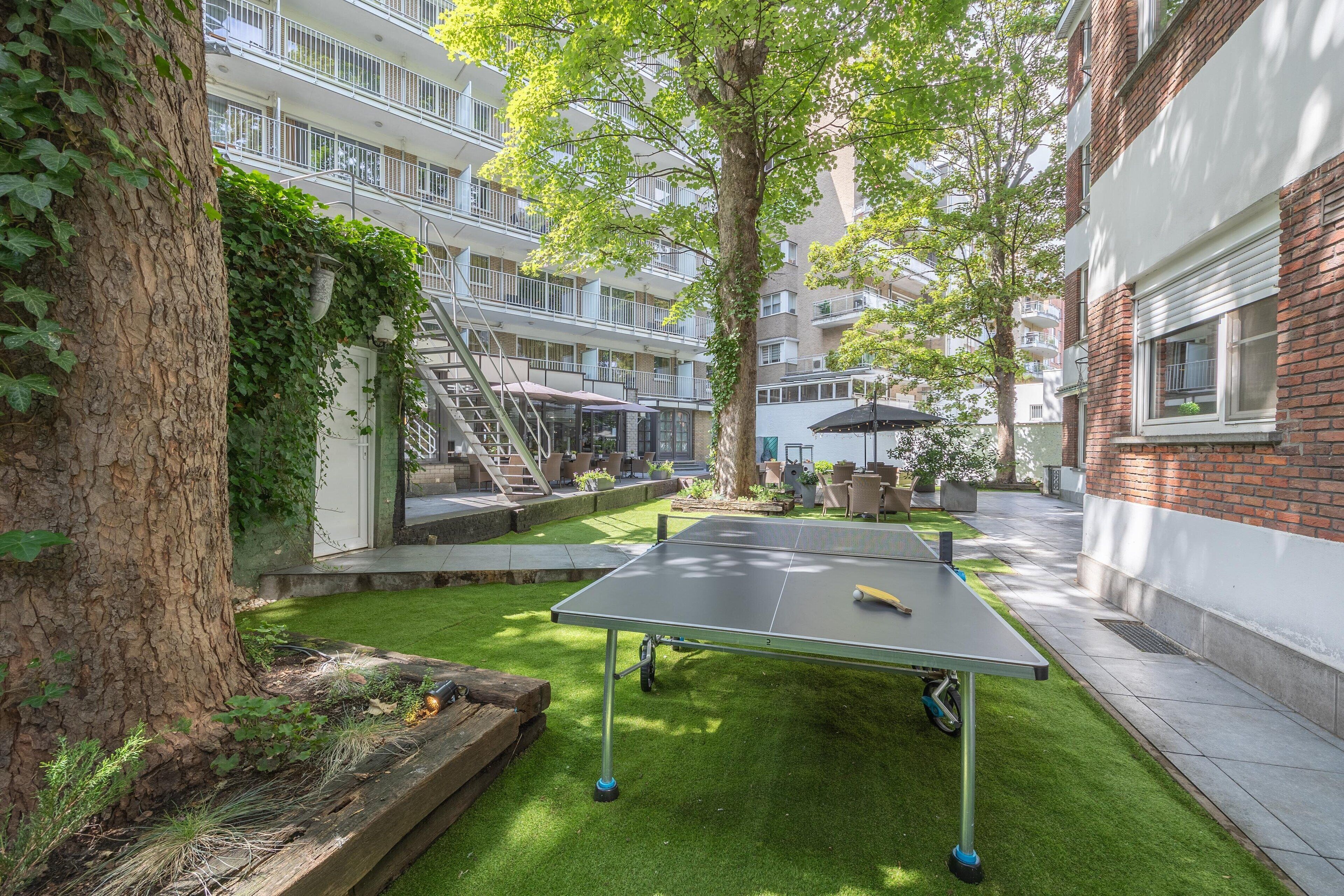 Un patio exterior con mesa de ping pong, un árbol y un edificio con balcones.