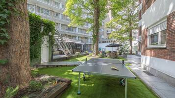 Un patio exterior con mesa de ping pong, un árbol y un edificio con balcones.