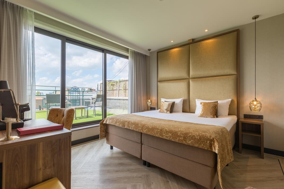A modern hotel room with a large bed, a desk, and a view of the outdoors.