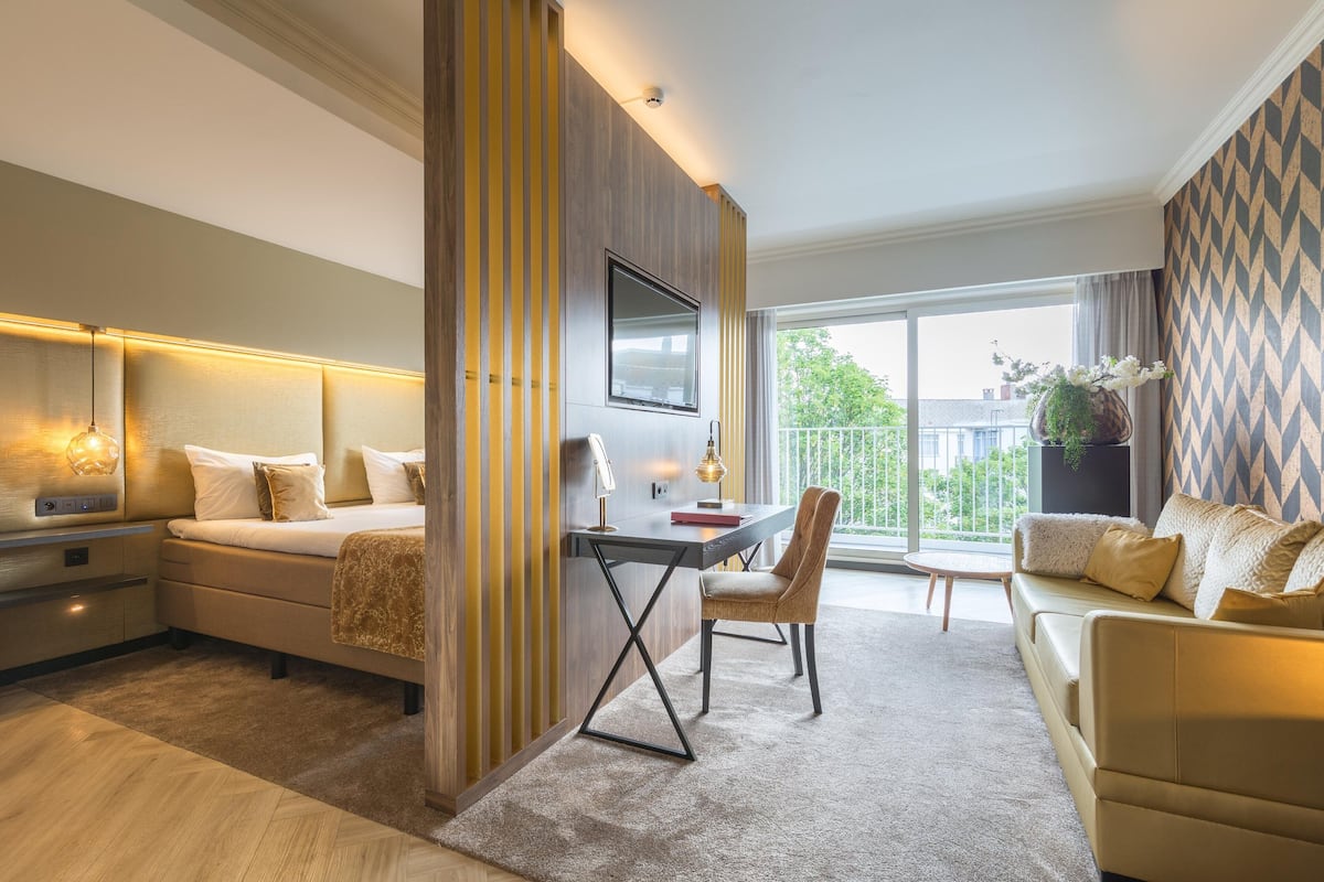 Une chambre moderne avec un lit, un bureau et une chaise, une grande fenêtre et une vue sur l’extérieur.