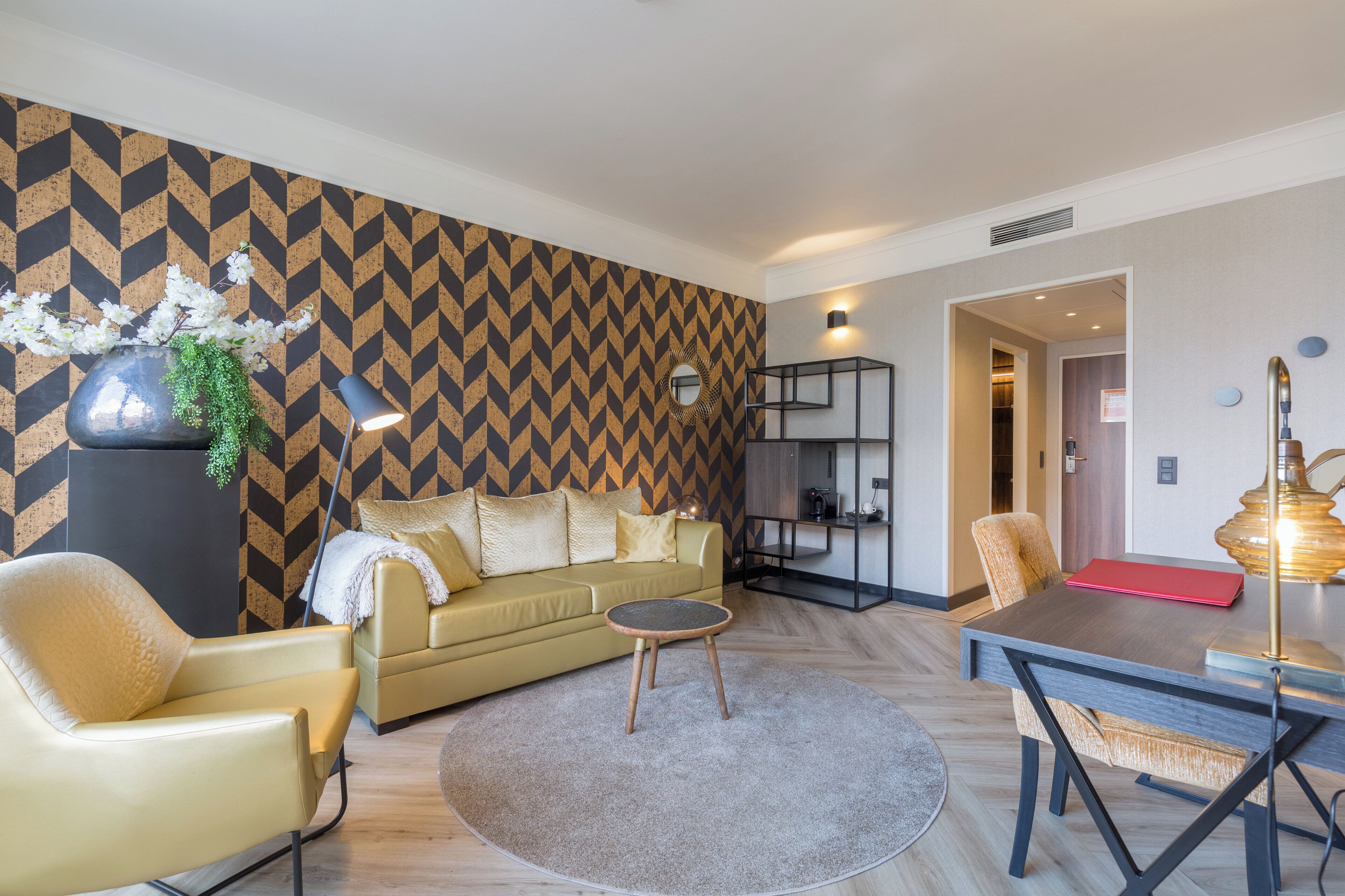 Ein modernes Wohnzimmer mit Wandpaneelen im geometrischen Muster, einer Couch, einem Couchtisch und einem Essbereich mit einer Lampe.