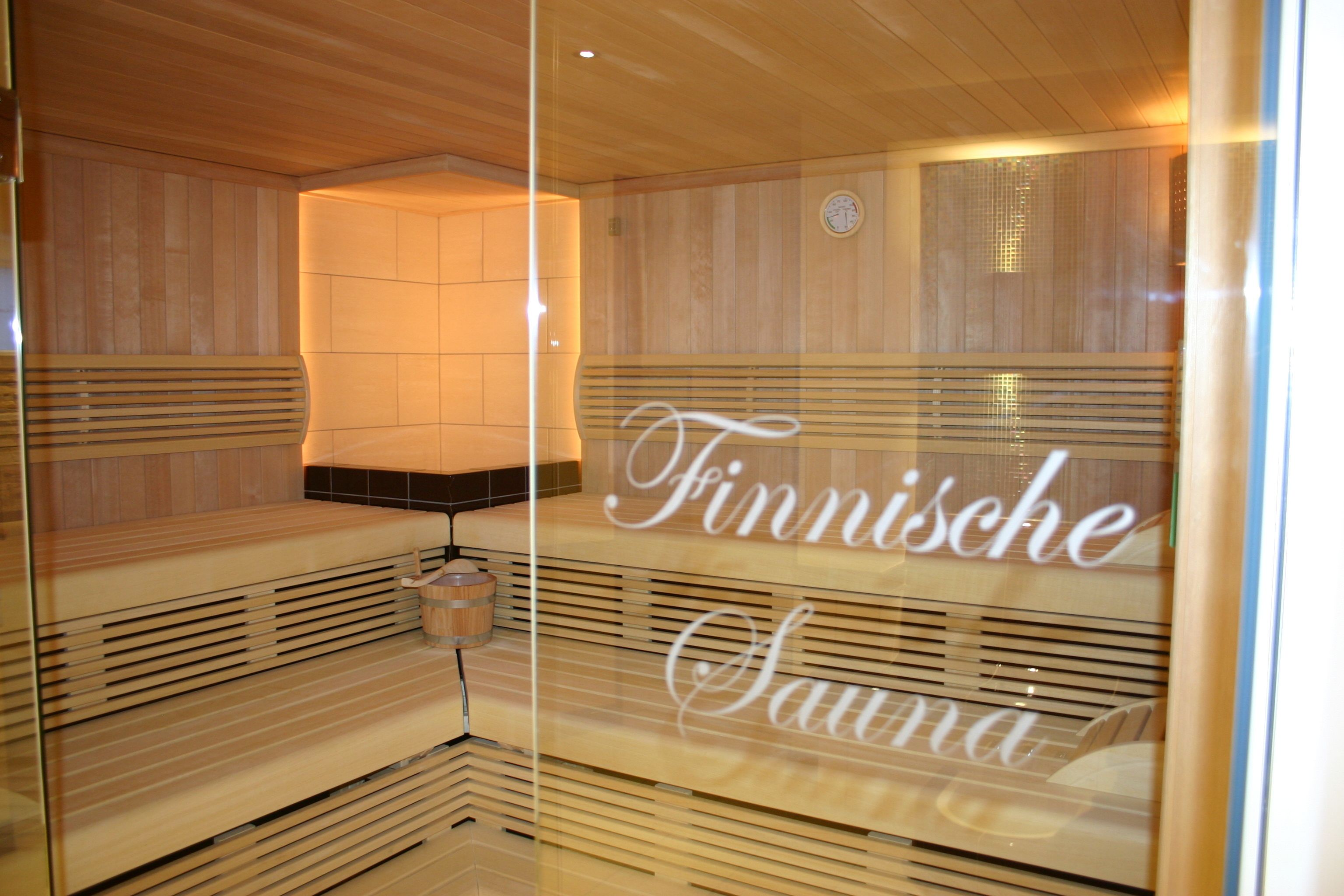 Una sauna con bancos de madera y una pared de vidrio que muestra el nombre "Finnische Sauna".