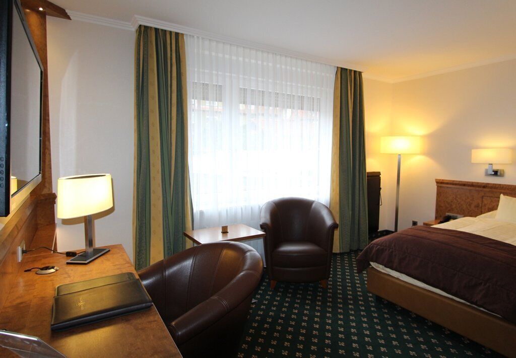 Ein Hotelzimmer mit einem Bett, einem Schreibtisch mit Lampe, einem Sessel und einem Nachttisch.