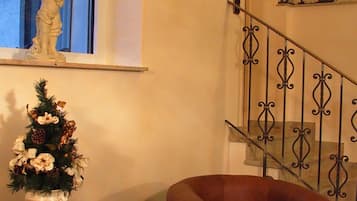 Una escalera con pared de piedra, una estatua en un estante, un árbol de Navidad y un sillón de cuero.