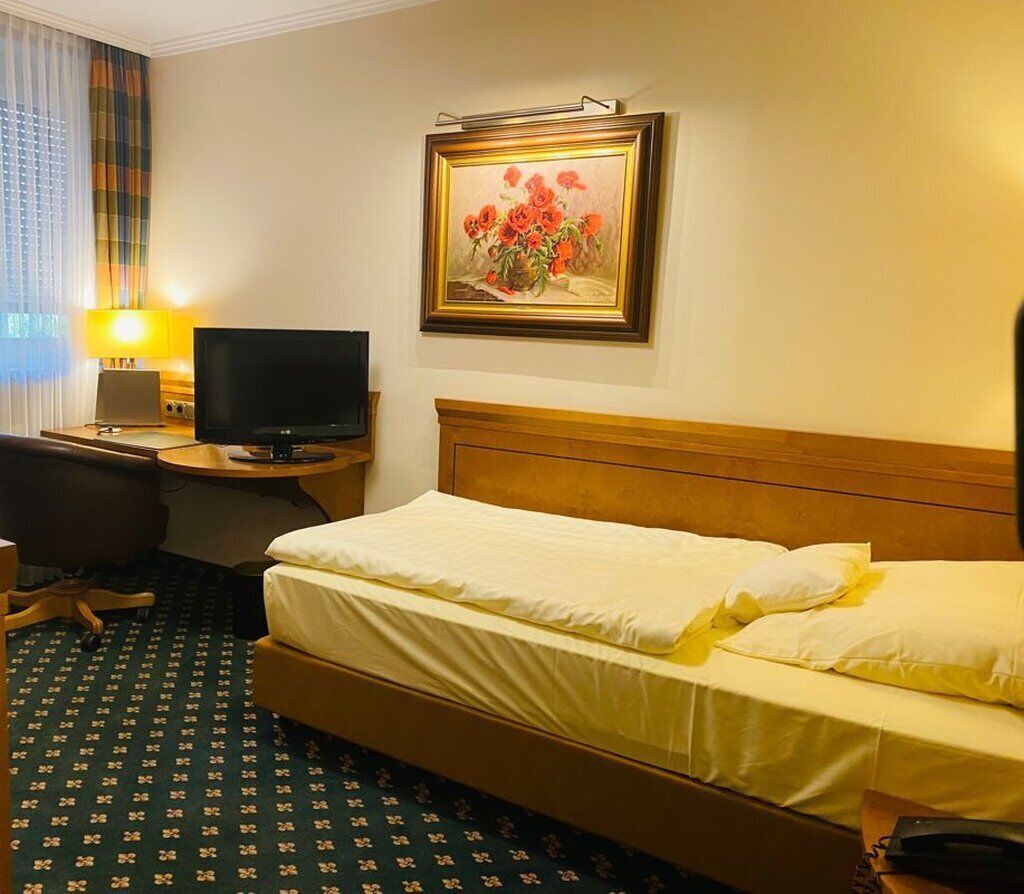 A hotel room with a bed, a desk with a television, a lamp, and a framed painting on the wall.