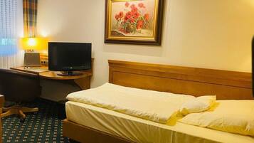 A hotel room with a bed, a desk with a television, a lamp, and a framed painting on the wall.