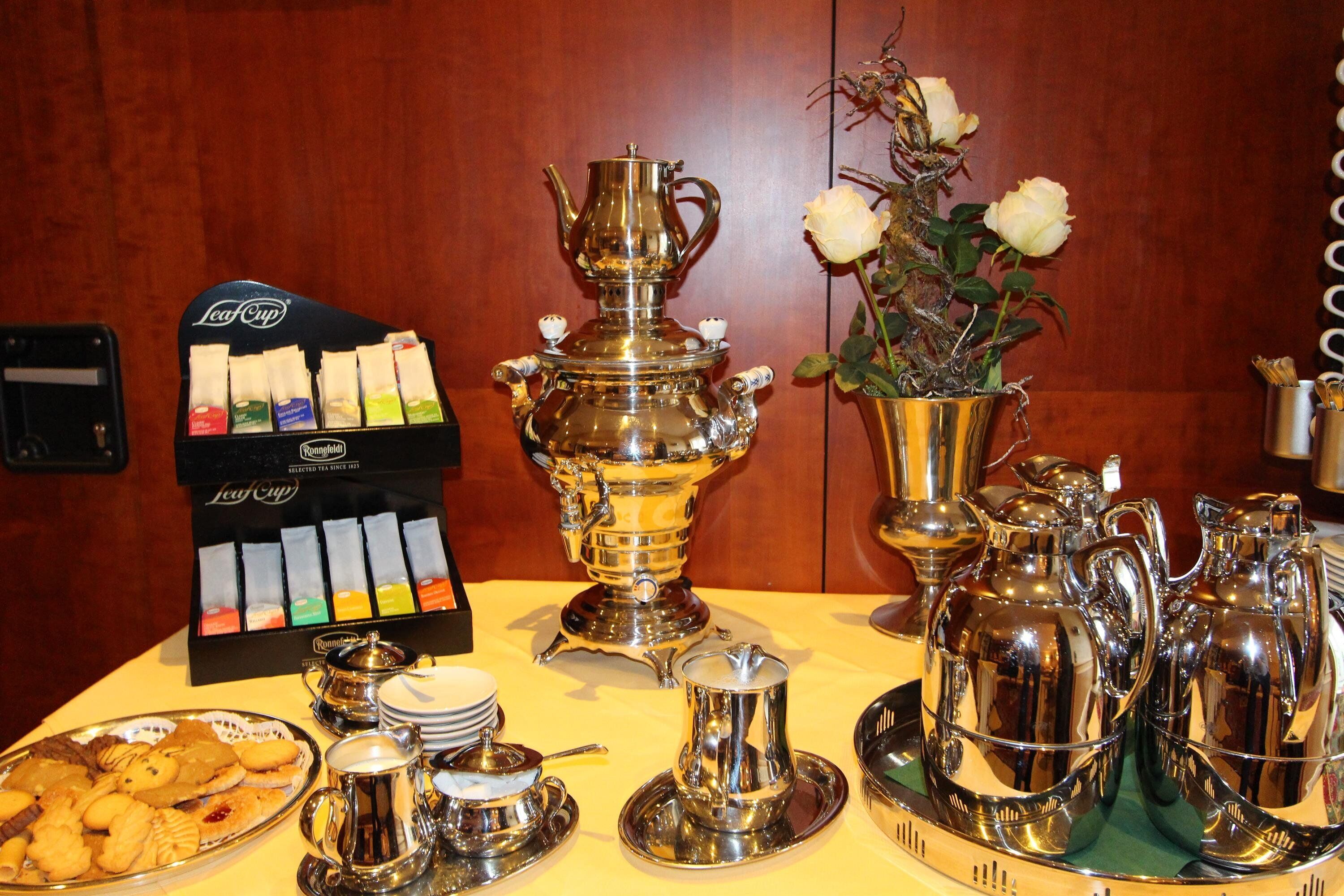 A breakfast table with tea bags, a samovar, teapots, cups, and a vase with flowers.