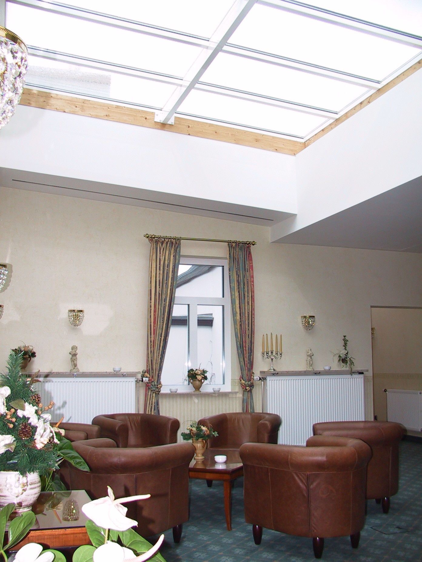 Un salón amplio con techo alto y tragaluces, con sillones de cuero, una mesa de centro de madera y un gran ventanal con cortinas.