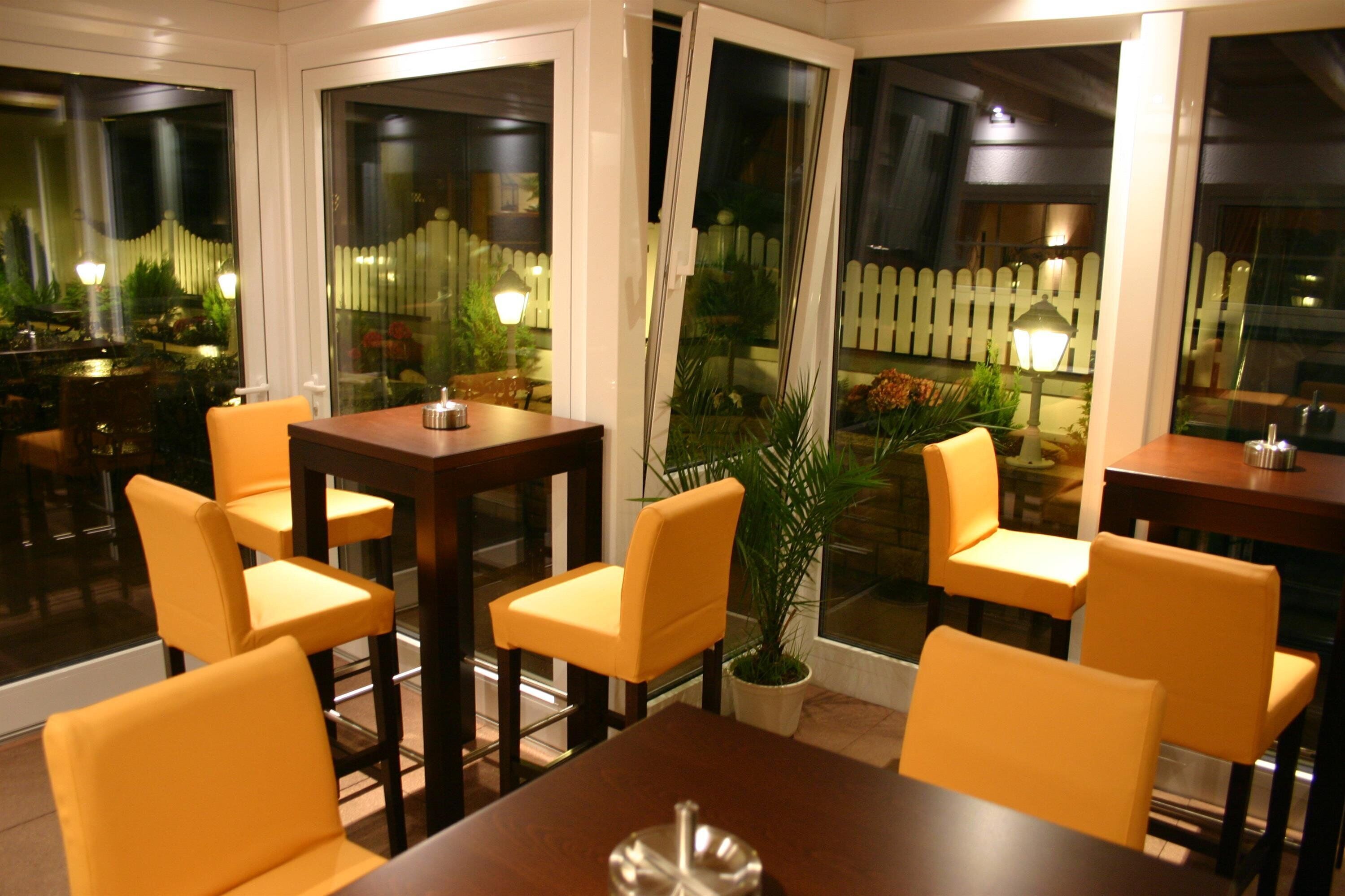 Un comedor con sillas amarillas y una mesa de madera, ventanas amplias con vistas a un jardín y una valla de piquetes blancos.