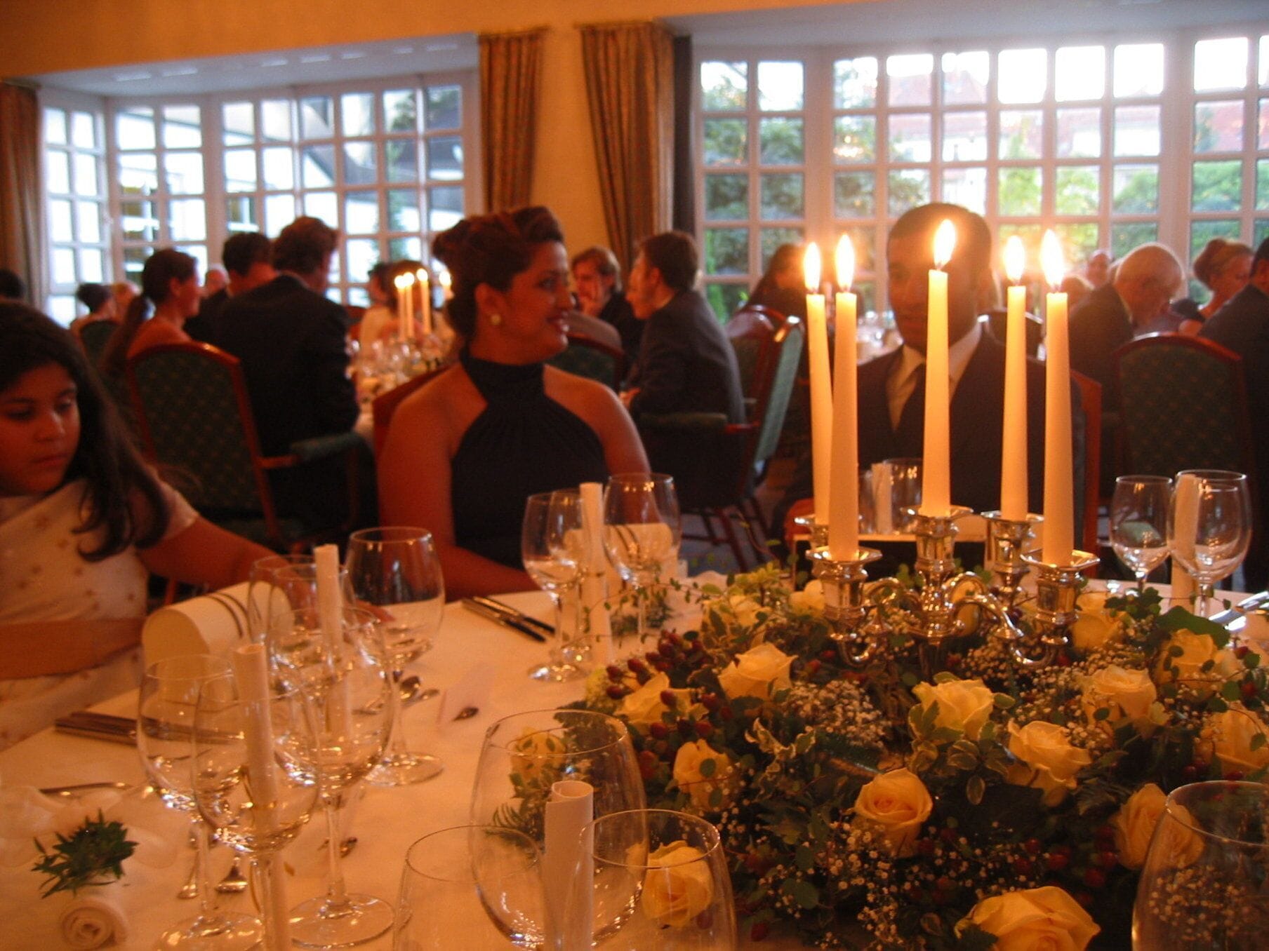 Un comedor con mesas dispuestas para un evento formal, con velas y centros de mesa florales.