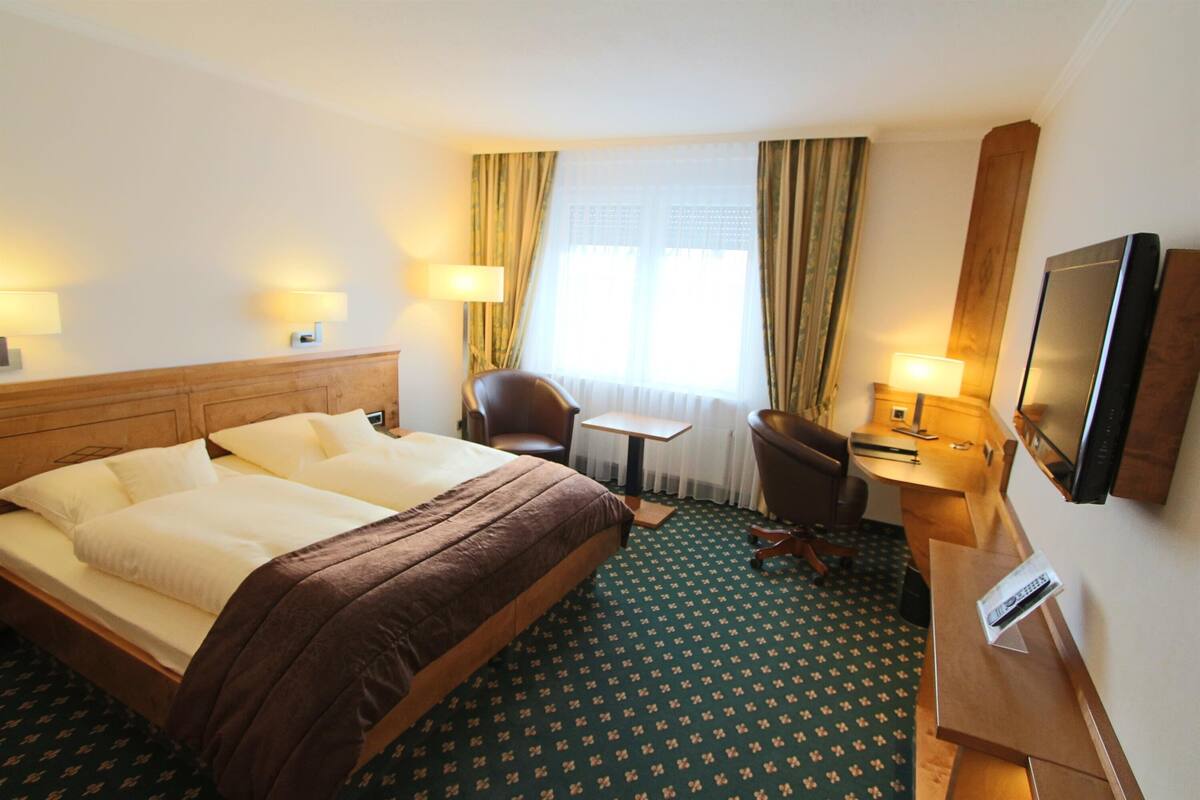 A hotel room with a large bed, a desk, a chair, and a TV.