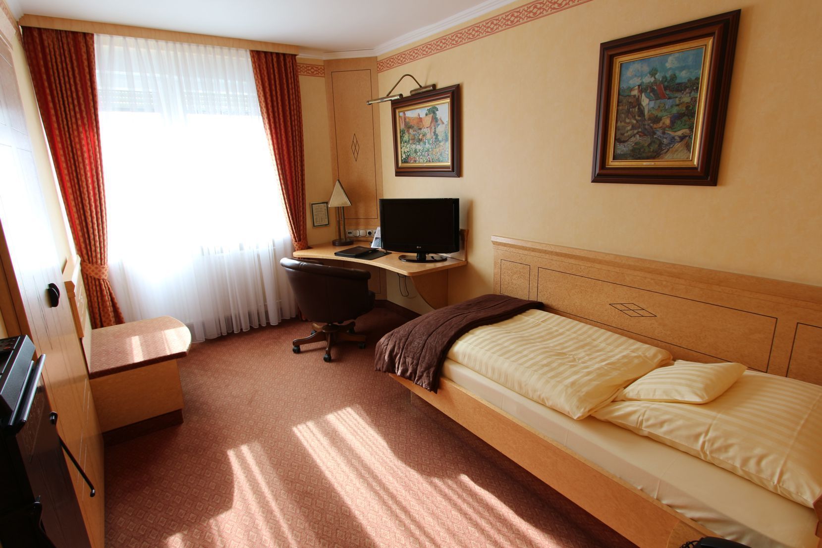 Una habitación de hotel con cama, escritorio, computadora y dos cuadros en la pared.