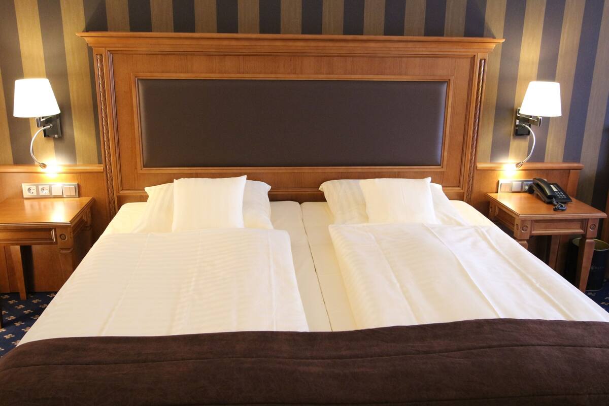 A hotel room with two beds, a wooden headboard, bedside lamps, a telephone, and a wall-mounted light switch.