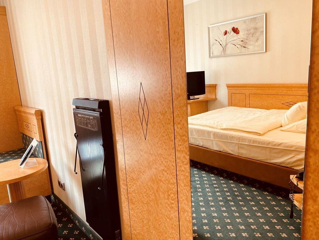 Quarto de hotel com cama, escrivaninha, cadeira, televisão e guarda-roupa.