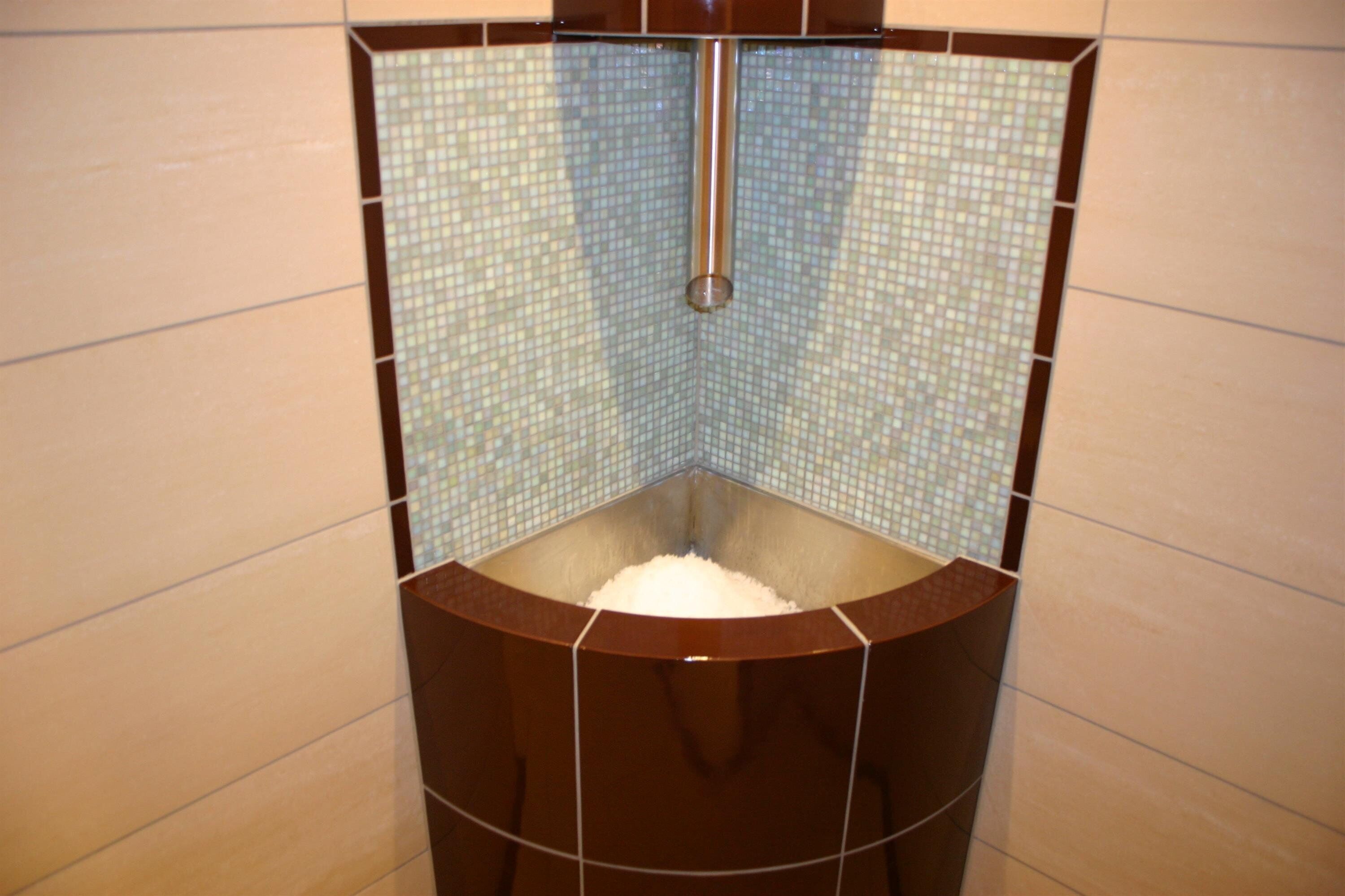Eine Eckdusche mit gefliestem Wandbereich und zentralem Ablauf.