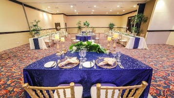Un salón de banquetes con mesas redondas cubiertas con manteles azules, sillas doradas y centros de mesa florales.