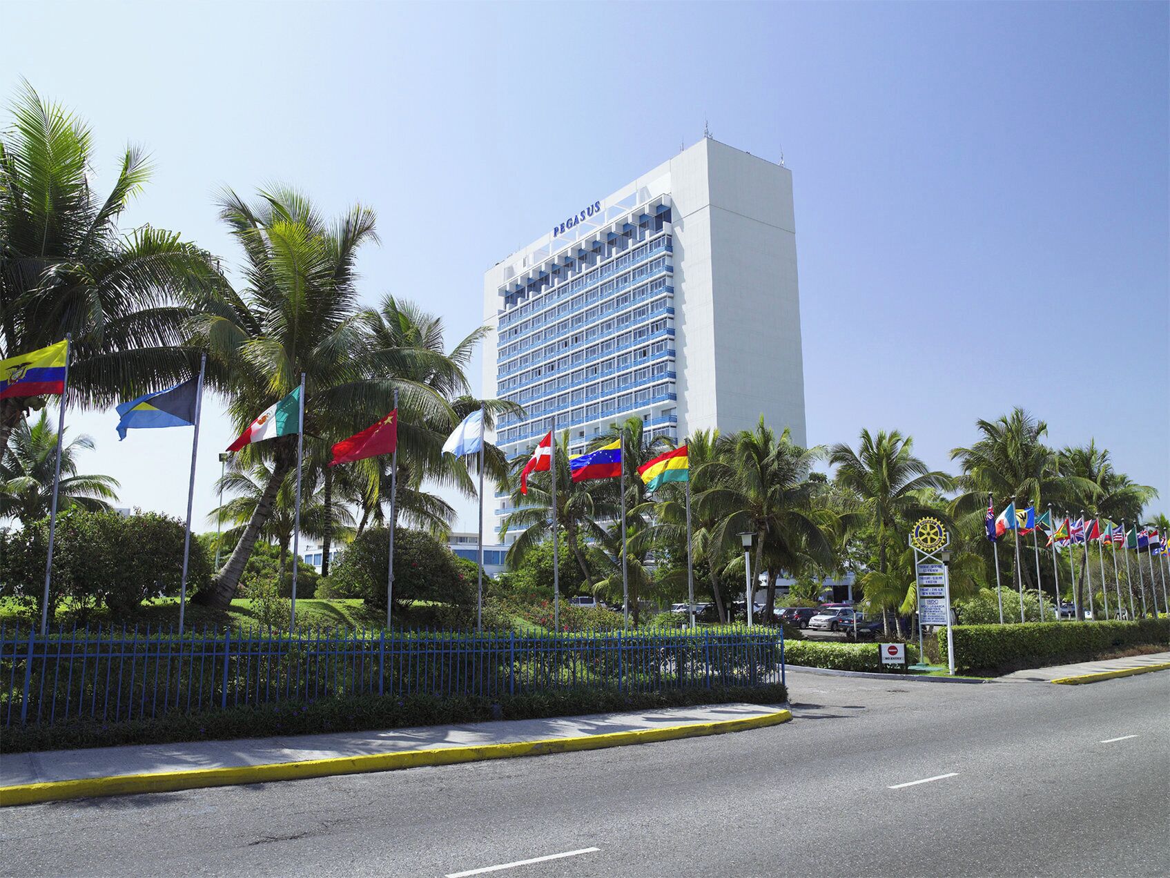 A hotel with multiple flags, a blue fence, and a clear sky.